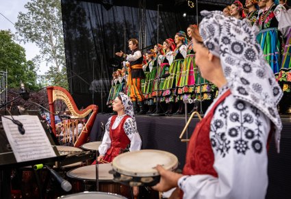 Na pierwszym Planie dwie Artystki z Orkiestry w kostiumach wilanowskich, grające na instrumentach, w tle Chór wraz z solistą w kostiumach łowickich