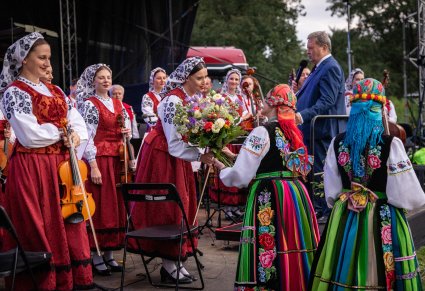 Artystki Chóru w kostiumach łowickich przekazują kwiaty Artystce Orkiestry, która ma na sobie kostium wilanowski