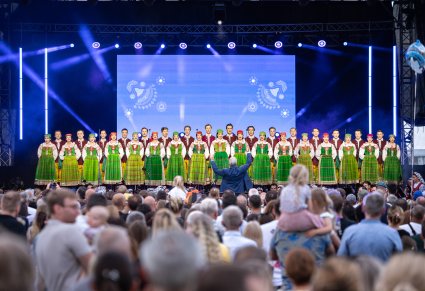 Widok z perspektywy publiczności, na cały chór w kostiumach kurpiowskich, wraz z dyrygującym Dyrektorem zespołu
