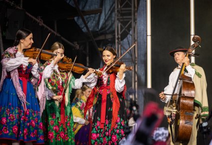 Muzycy orkiestry, grający na instrumentach smyczkowych, w kostiumach podhalańskich, podczas gry na scenie