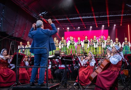 Dyrygujący Dyrektor zespołu, orkiestra w kostiumach wilanowskich, powyżej solistki i reszta chóru, wykonująca "Dwa serduszka"
