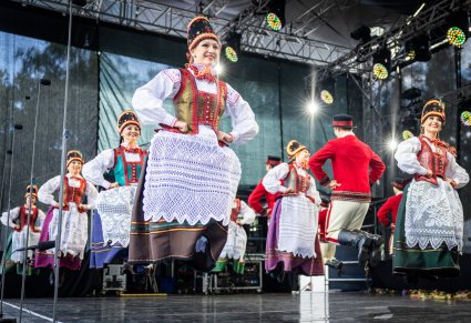 Grupa Artystów w kostiumach kurpiowskich w trakcie wykonywania choreografii tanecznej na scenie