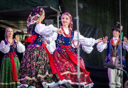 Na pierwszym planie Artystki w kostiumach limanowskich w trakcie wykonywania choreografii tanecznej, na drugim planie pozostali Artyści