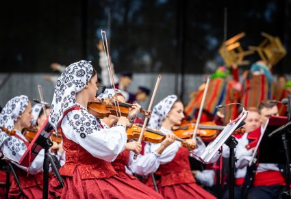 Na pierwszym planie skrzypaczki a w tle Artyści w kostiumach sieradzkich w trakcie wykonywania choreografii