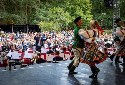 Na pierwszym planie para Artystów w kostiumach spiskich w trakcie wykonywania choreografii tanecznej w tle widoczna Orkiestra w kostiumach wilanowskich wraz z Dyrygentem i Publiczność