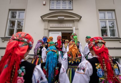 Widok z tyłu na chórzystki w kostiumach łowickich, wchodzące do Pałacu Karolin