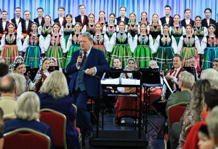 Przemawiający Dyrektor zespołu, w tle chór w kostiumach łowickich