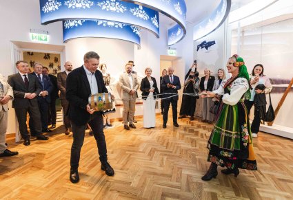 Przewodniczka w kostiumie łowickim wraz z uczestnikiem Konwentu próbują swoich sił w grze na instrumencie regionalnym, w tle Uczestnicy Konwentu