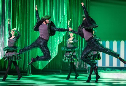 Dwóch Artystów w kostiumach zielono, szaro, czarnych odgrywający rolę Kół w trakcie wykonywania imponującej choreografii tanecznej