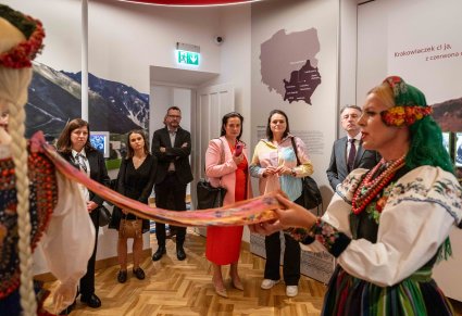 Na pierwszym planie Przewodniczka w kostiumie łowickim prezentująca detale na kostiumie krakowskich, w tle widoczni uczestnicy Konwentu Przewodniczących Sejmików Województw RP