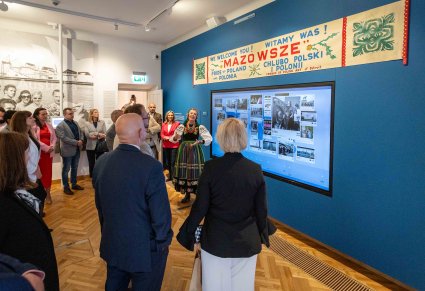 Uczestnicy Konwentu Przewodniczących Sejmików Województw RP w trakcie zwiedzania wystawy z przewodniczką, przewodniczka ma na sobie kostium łowicki