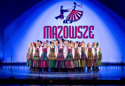 Ba scenie Artyści w kostiumach opoczyńskich a na tle sceny widoczne duże logo zespołu "Mazowsze"