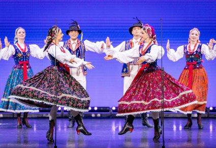 Na pierwszym planie Artystki w kostiumach limanowskich w trakcie wykonywania choreografii tanecznej  w tle pozostała grupa Artystów