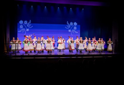 Grupa Artystów w kostiumach krakowskich w trakcie śpiewu i grania na instrumentach na scenie