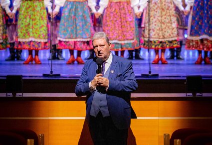 Dyrektor zespołu podczas przemowy do Publiczności, w tle na scenie Artyści w kostiumach krakowskich