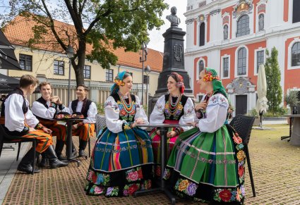 Artyści w kostiumach łowickich a w tle Pomnik Stanisława Moniuszki  przy kościele św. Katarzyny