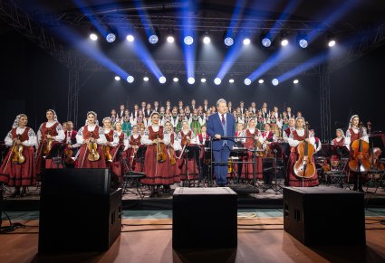 Na pierwszym planie Dyrektor zespołu w roli Dyrygenta, za nim Orkiestra w kostiumach wilanowskich oraz Artyści Chóru w kostiumach łowickich