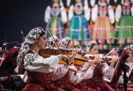 Na pierwszym planie Artystka Orkiestry w kostiumie wilanowskim w trakcie gry na skrzypcach