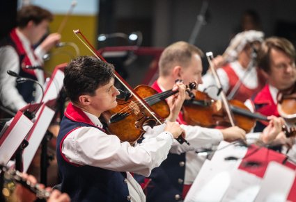 Zbliżenie na Artystę Orkiestry w kostiumie wilanowskim, grającego na instrumencie smyczkowym