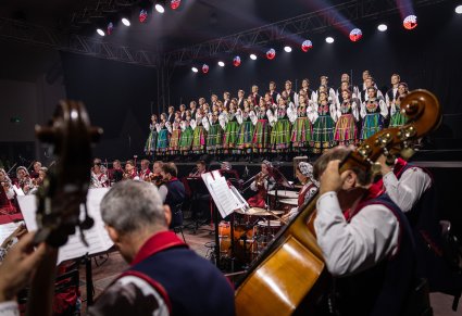 Na pierwszym planie Artyści Orkiestry w kostiumach wilanowskich, w tle na scenie Artyści Chóru w kostiumach łowickich