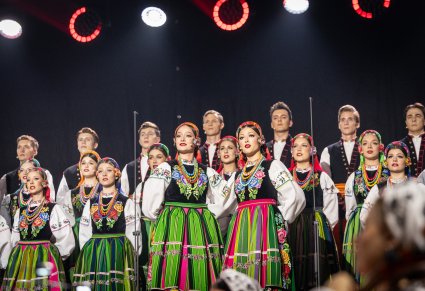 Zbliżenie na Solistki, za nimi Artyści Chóru w kostiumach łowickich