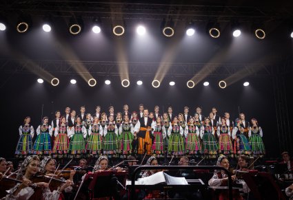 Solista wykonujący utwór "Furman" na tle Artystów Chóru w kostiumach łowickich, niżej sceny widoczna część Orkiestry w kostiumach wilanowskich