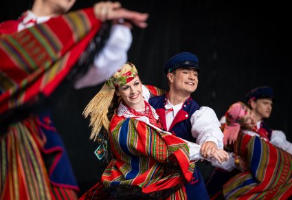 Pary Artystów w kostiumach sieradzkich na scenie wykonujące choreografię taneczną