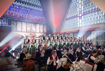 Perspektywa boczna na Artystów Chóru w kostiumach łowickich w trakcie śpiewu oraz Artyści Orkiestry w kostiumach wilanowskich
