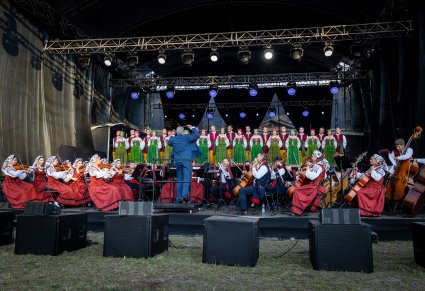 Na pierwszym planie Orkiestra z Dyrygentem a w tle na scenie Chór w kostiumach kurpiowskich