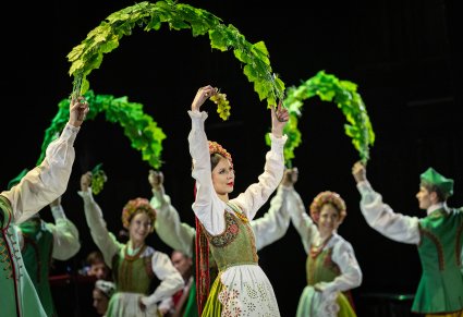 Grupa Artystów w kostiumach lubuskich w trakcie wykonywania choreografii tanecznej. Artyści trzymają w górze winorośla.