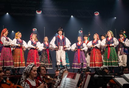 Na scenie Artyści w kostiumach limanowskich w trakcie gry na instrumentach ludowych, niżej część orkiestry w kostiumach wilanowskich