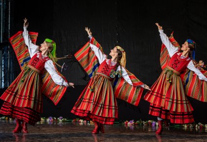 Trzy artystki na scenie w kostiumach sieradzkich wykonujące choreografię taneczną