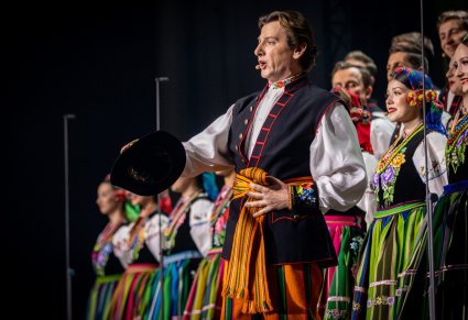 Zbliżenie na solistę chóru w kostiumie łowickim podczas koncertu z widocznych chórem w tle