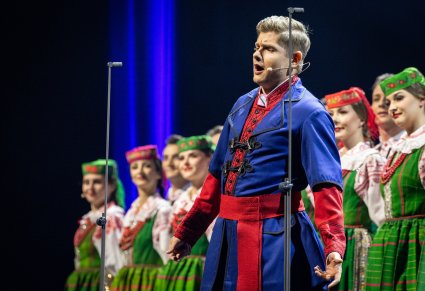 Zbliżenie na Solistę w kostiumie kujawski, na drugim planie za nim Artyści Chóru w kostiumach kurpiowskich