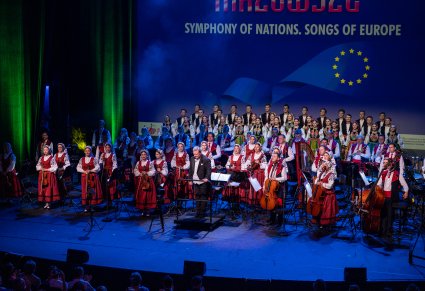 Na pierwszym planie Dyrektor Jacek Boniecki w trakcie ukłonu w stronę publiczności, za nim Orkiestra i chór w rzędach w kostiumach łowickich