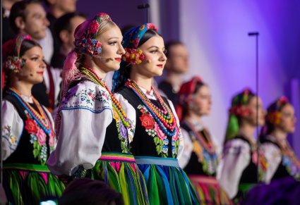 Zbliżenie na dwie solistki w kostiumach łowickich, w tle część Artystów Chóru