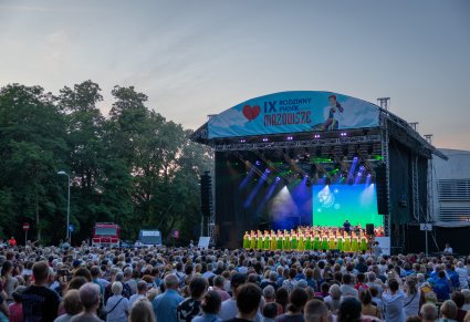 Widok na główną scenę plenerową na której znajdują się Artyści Chóru w kostiumach kurpiowskich, a na tyłach sceny Orkiestra w kostiumach wilanowskich wraz z Dyrygentem