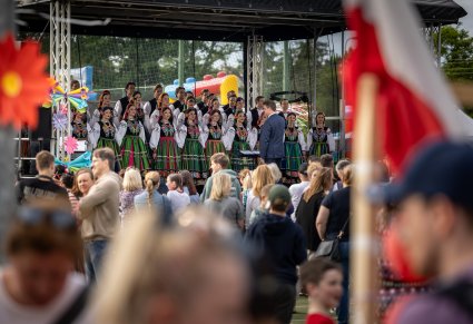 Widok na większą część sceny i Publiczność. Na scenie Dyrygent zwrócony w stronę Artystów Chóru, ubranych w kostiumy łowickie