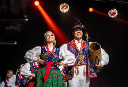 Na pierwszym planie uśmiechnięta para Artystów na scenie w kostiumach limanowskich