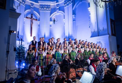 Widok na Chór w kostiumach łowickich stojący przed ołtarzem a przed nim część orkiestry w kostiumach wilanowskich