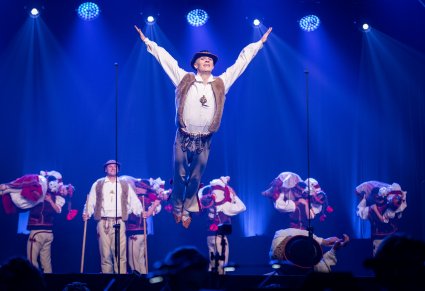 Tancerz w kostiumie jurgowskim podczas akrobacji tanecznych, w tle widoczni inni tancerze