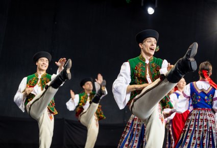 Grupa Artystów w kostiumach spiskich w trakcie wykonywania choreografii tanecznej na scenie