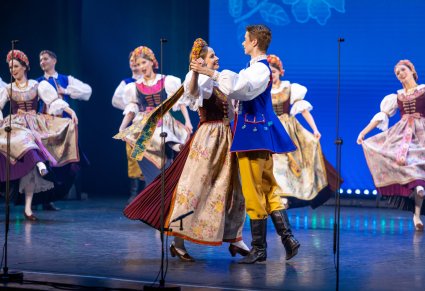 Na pierwszym planie para Artystów w kostiumach rozbarskich w trakcie wykonywania choreografii tanecznej, za nimi reszta część Artystów Baletu
