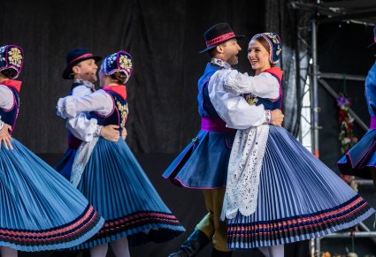Pary Artystów w kostiumach kaszubskich na scenie wykonujący choreografię taneczną