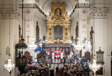 Szeroki kadr na Kościół Św. Krzyża w Warszawie, widok na bogato zdobiony ołtarz na którym znajduję się Arcybiskup z duchownymi, Dyrygent zespołu "Mazowsze" wraz z Orkiestrą i Chórem