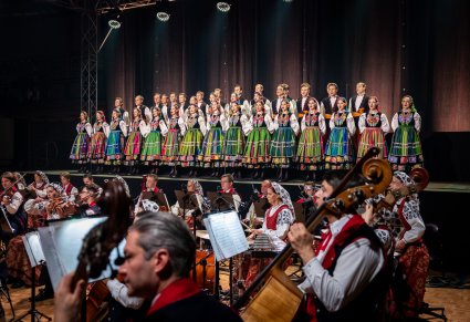 Część orkiestry w kostiumach wilanowskich a w tle na scenie chór w kostiumach łowickich podczas śpiewu