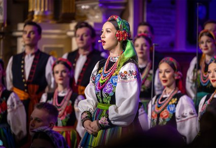 Zbliżenie na solistkę chóru podczas koncertu z widocznych chórem w tle