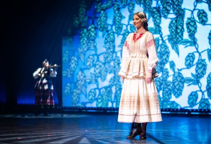 Artystka w ślubnym kostiumie krzczonowskim stojąca na scenie, w tle widoczna skrzypaczka