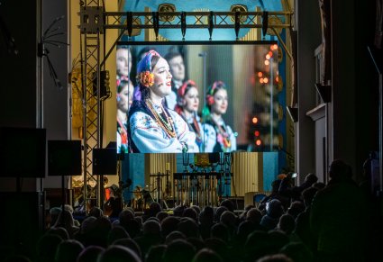 Widok na telebim z Artystami Chóru, widoczna orkiestra koncertu