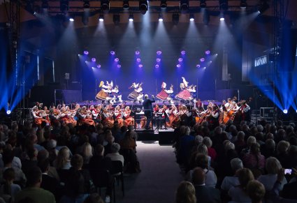 Na scenie Artyści Baletu w kostiumach limanowskich w trakcie wykonywania choreografii tanecznej, niżej Artyści Orkiestry w kostiumach wilanowskich oraz widoczna część Publiczności